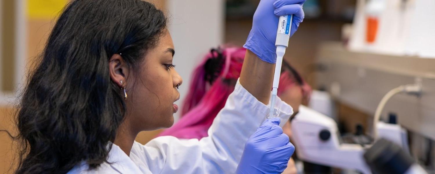 SPU的学生在实验室工作, 向试管中加入液体, 她的同学在后台工作.